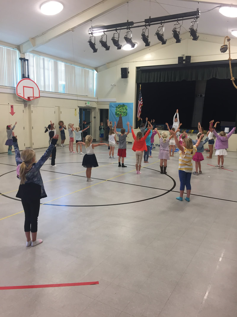 students performing tree yoga pose in the gym with a parent volunteer leader