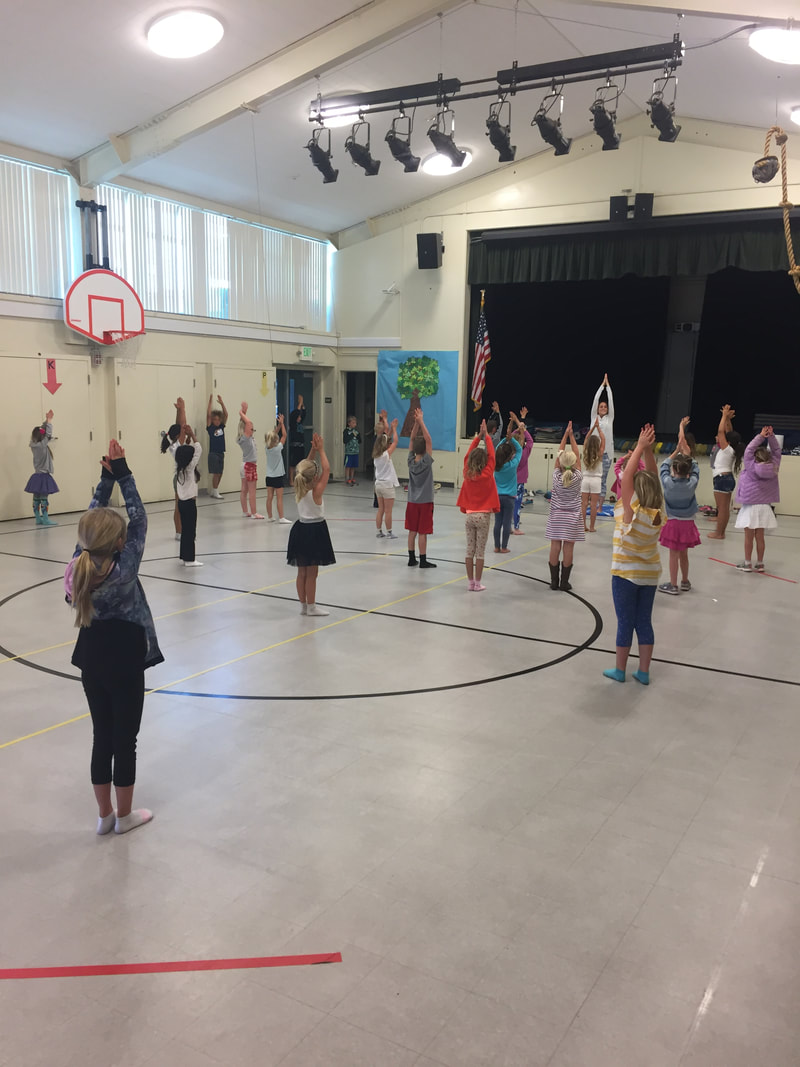 students performing tree yoga pose in the gym with a parent volunteer leader