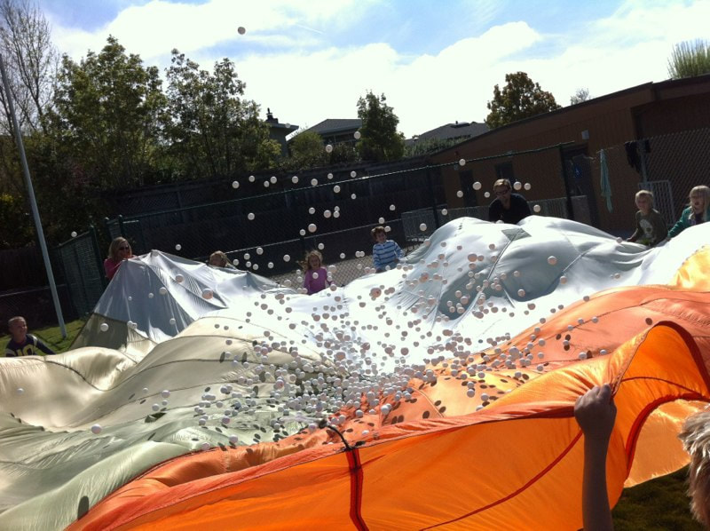 Students shaking a very large parachute with 1,000 ping pong balls bouncing wildly like popcorn